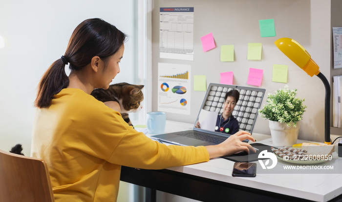 Young Asian woman holding cat working from home due to coronavirus covid-19, making online video call with colleague, Work from home concept