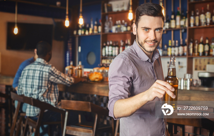 Handsome young man holding beer bottle and smiling