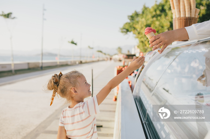 Cute little girl standing near ice cream shop buying ice cream cone.