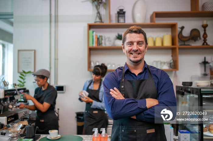 Portrait of smiling owner man standing at his cafe. Coffee owner standing with apron in coffee shop to welcome customer.