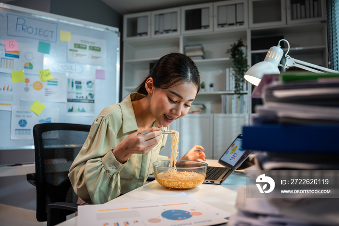 Asian young businesswoman eating noodles while work in office at night.