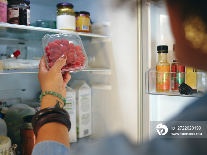 Woman finding box of raspberries in fridge, close up