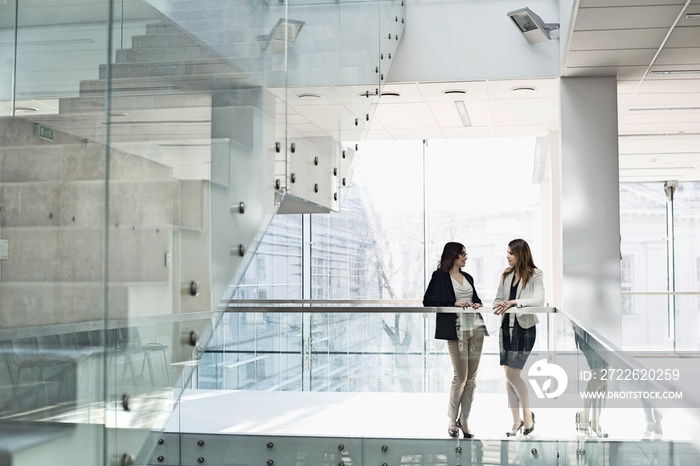 Businesswomen conversing against railing in office