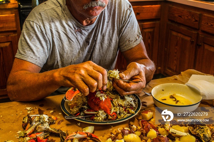 Older man with very strong looking hands eating a crab at a seafood boil