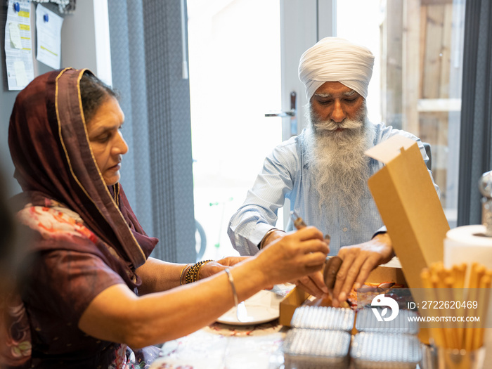 Senior couple in traditional clothing eating pizza at home