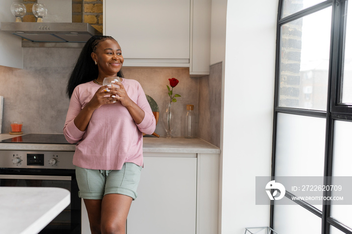 Portrait of smiling woman standing and looking through kitchen window