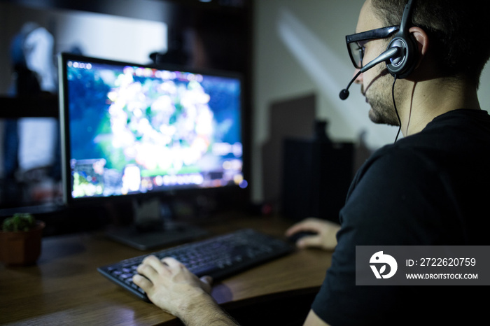 night play. young gamer in headphones and glasses using computer for playing game at home