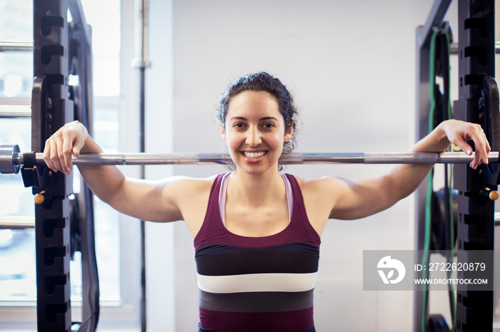 Portrait of smiling female athlete with barbell standing against wall in gym