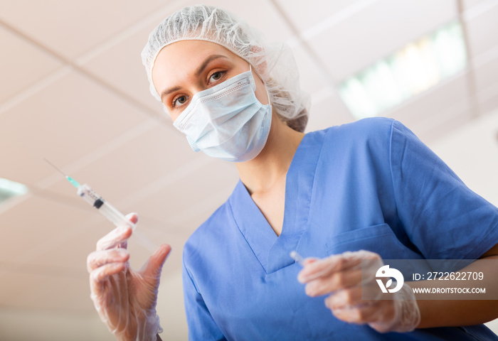 Female nurse in mask holding syringe for injection in hospital