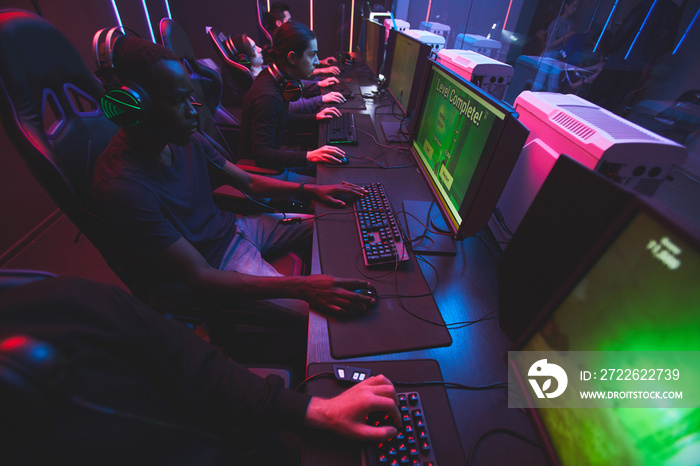 Group of concentrated young multi-ethnic people sitting on row and playing computer games online