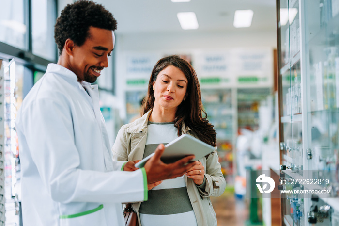 Pharmacist using digital tablet with customer.