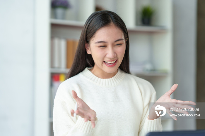 Beautiful young Asian woman college student is video chatting with her classmates using laptop, smiling faces and gestures happily studying.