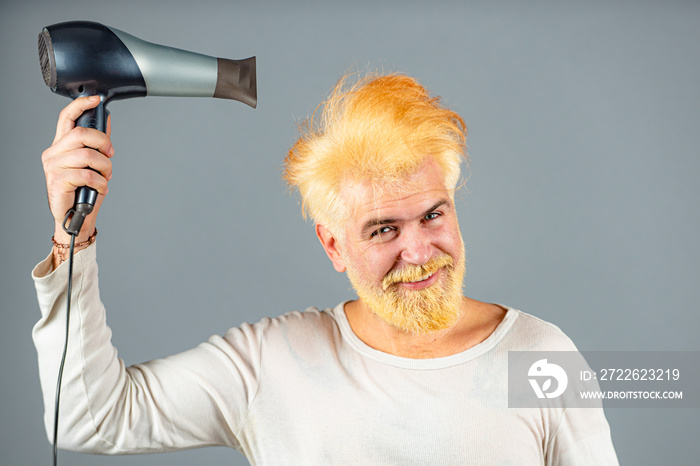 Handsome redhead man with long hair dries his hair with a hairdryer. Blonde man with hair dryer.