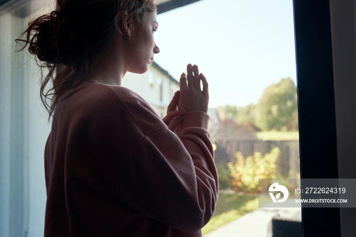 Thoughtful depressed young woman looking through the window