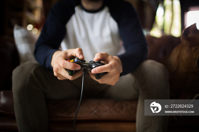 A young man holding joystick, playing video game. Man sitting on sofa, playing video games on console.