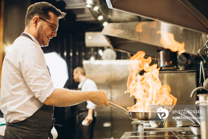 Man chef frying meat in a pan in fire