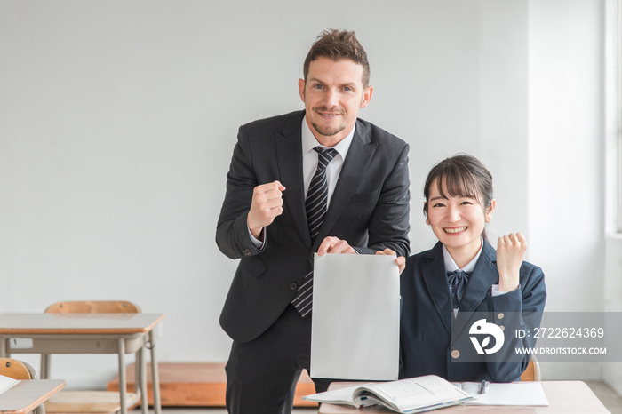 学校の教室でテストの答案用紙をもつ中学生・高校生と先生