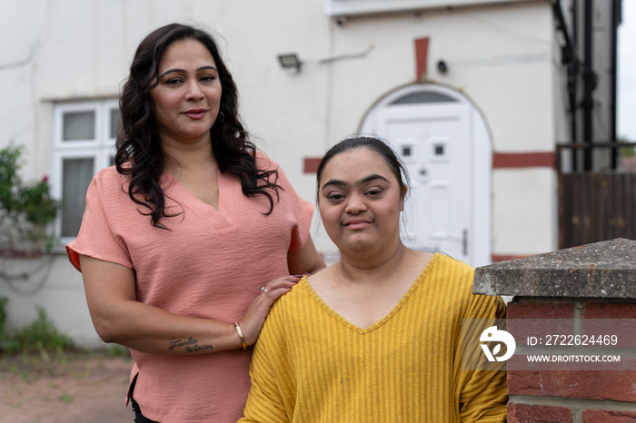 Portrait of woman with down syndrome daughter standing in front of house