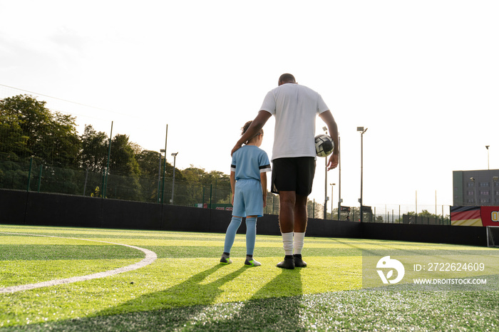 Rear view of coach and girl (6-7) on soccer field