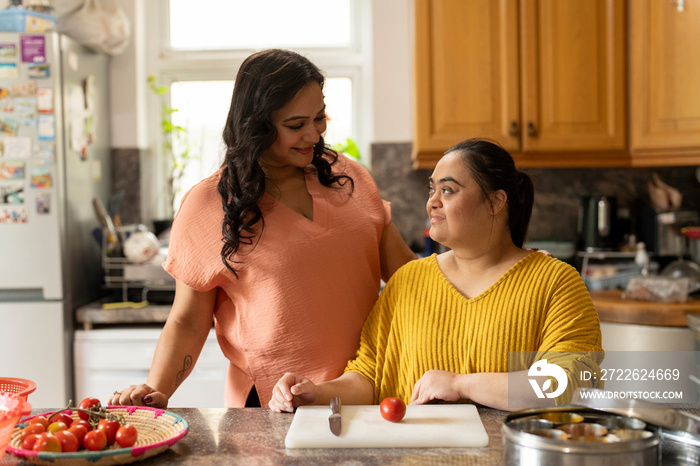 Portrait of mother with down syndrome daughter preparing food in kitchen