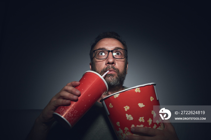 Adult man watching movies at home, eating popcorn and drinking juice.