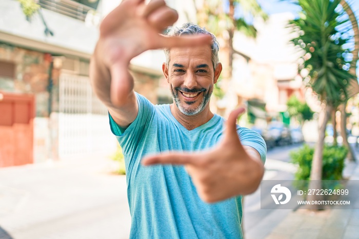 Middle age grey-haired man wearing casual clothes at street of city smiling making frame with hands and fingers with happy face. creativity and photography concept.