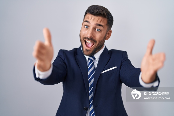 Handsome hispanic man wearing suit and tie looking at the camera smiling with open arms for hug. cheerful expression embracing happiness.