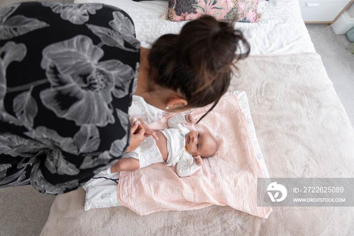 Mother changing diaper to newborn baby girl on bed at home