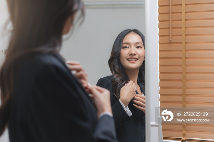 Confident, cheer up asian young woman standing in suit formal, getting dress for work looking at mirror at home before job interview of change career, recruitment employee or staff in company.