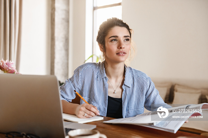 Image of candid pretty woman studying with textbooks and using laptop at home