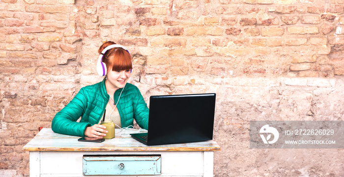 Young woman with headphones using laptop at house office - Remote smart working and technology concept due to isolation emergency of staying at home in quarantine - Bright filter with focus on girl