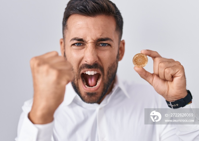 Handsome hispanic man holding cardano cryptocurrency coin annoyed and frustrated shouting with anger, yelling crazy with anger and hand raised