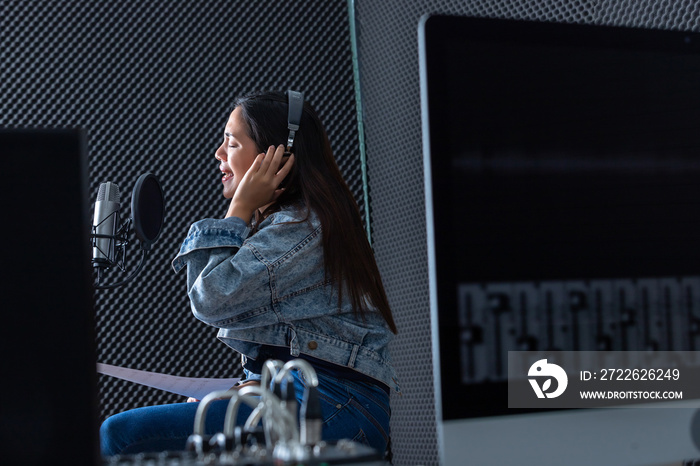 Happy cheerful pretty smiling of portrait of young Asian woman vocalist Wearing Headphones recording a song front of microphone in a professional studio