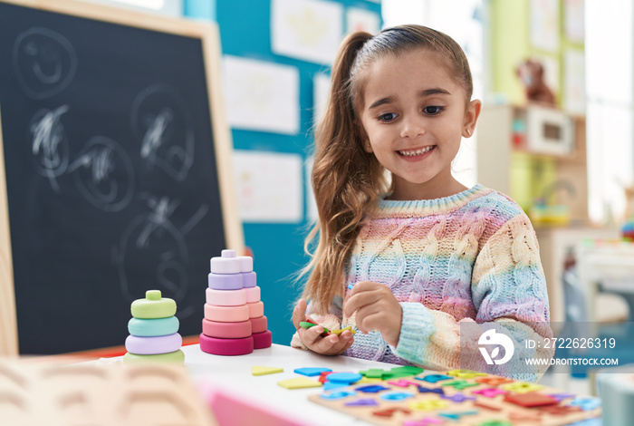 Adorable hispanic girl playing with maths puzzle game standing at kindergarten