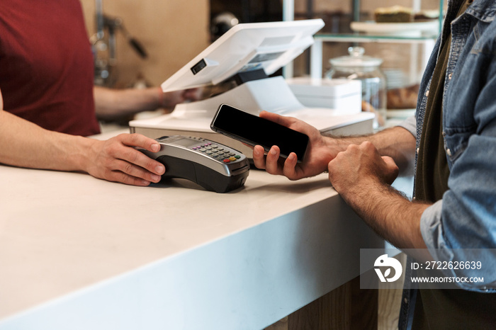 Photo of european man paying cellphone in cafe while waiter holding payment terminal