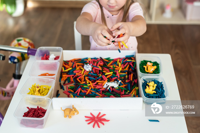 Little girl toddler playing with sensory bin with colored dyed pasta. Sensory play and learning colors activity for kids, material Montessori, games for fine motor skills, craft activities