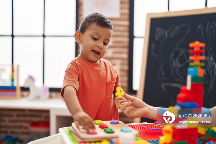 Adorable hispanic toddler playing with maths puzzle standing at kindergarten