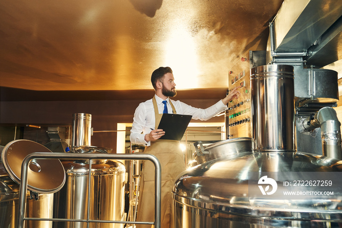 Handsome engineer of brewery inspecting process of brewing.