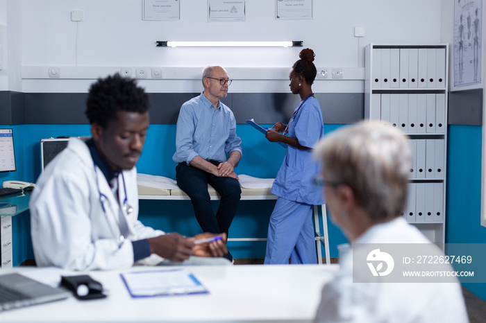 Hospital nurse conversating with senior man about consultation results and future examination appointment. Elderly man discussing with clinic nurse about treatment schedule.