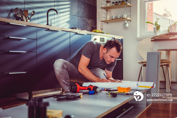 Man checking blueprints while building kitchen cabinets