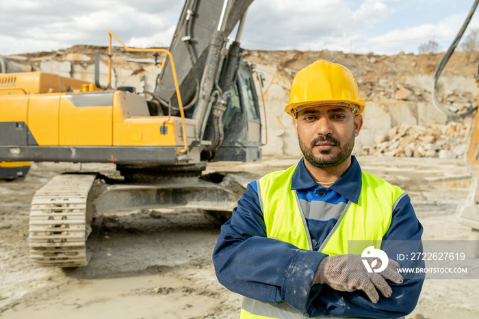 Serious builder in workwear crossing arms on chest against bulldozer