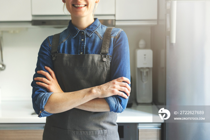 young smiling woman with apron standing in home kitchen with arms crossed