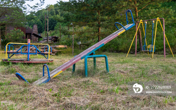 Old swings, abandoned playground equipment, on the background of swings and carousels.