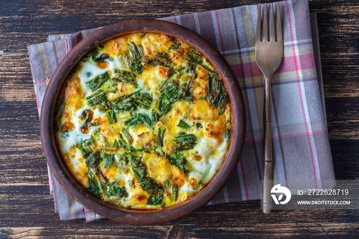 Ceramic bowl with vegetable frittata, simple vegetarian food. Frittata with egg, pepper, onion, cheese and green wild garlic leaves on table