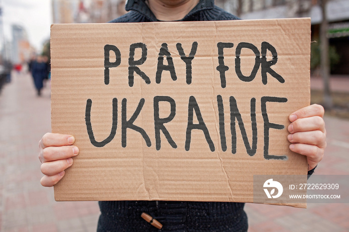 Middle aged civil man stands on crowded city street and holds a poster with anti-war message. Protest against the Russian intervention to Ukraine, activism and human rights movement