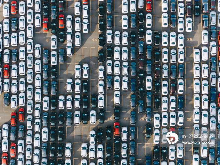 New multi-colored passenger cars stand in straight rows on a giant paved marked parking lot on the territory of an automobile manufacturing plant, overproduction