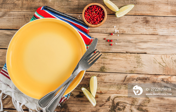 Festive Mexican table setting. Plate and cutlery with colorful napkin on rustic wooden background. Flat lay.