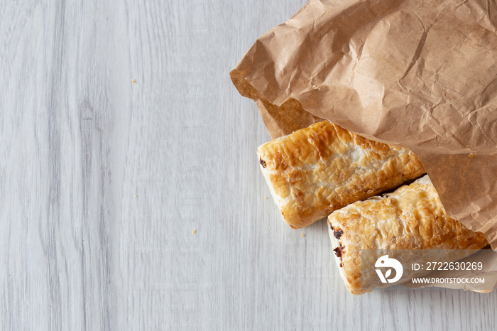 Sausage rolls in a brown paper bag, environmentally friendly biodegradable packaging, with a grey wood background