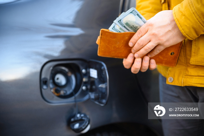 A hand holding a wallet full of cash near opened fuel car tank