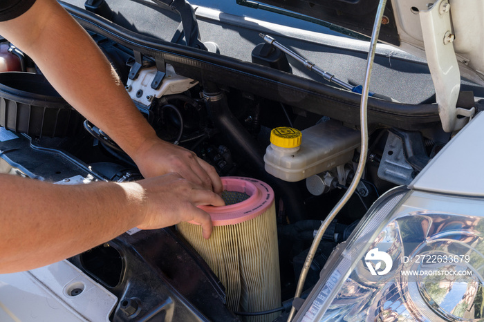 close up of hands of a caucasian male car mechanic changing the air filter in an engine